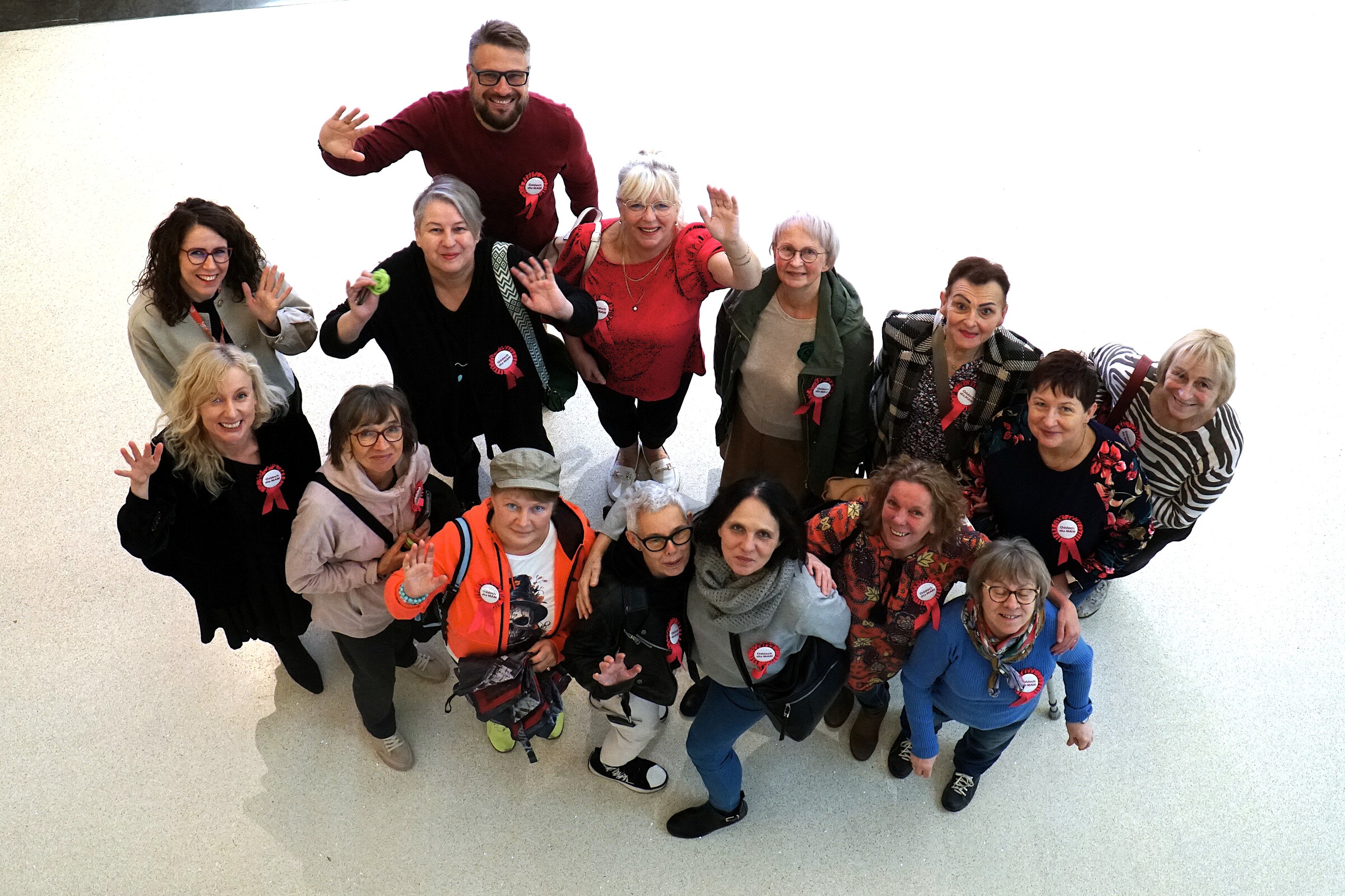 Grupa kobiet i jeden mężczyzna patrzą w górę i machają do aparatu. Zdjęcie wykonane z góry w galerii Posnania podczas wydarzenia Oddech dla Mam.